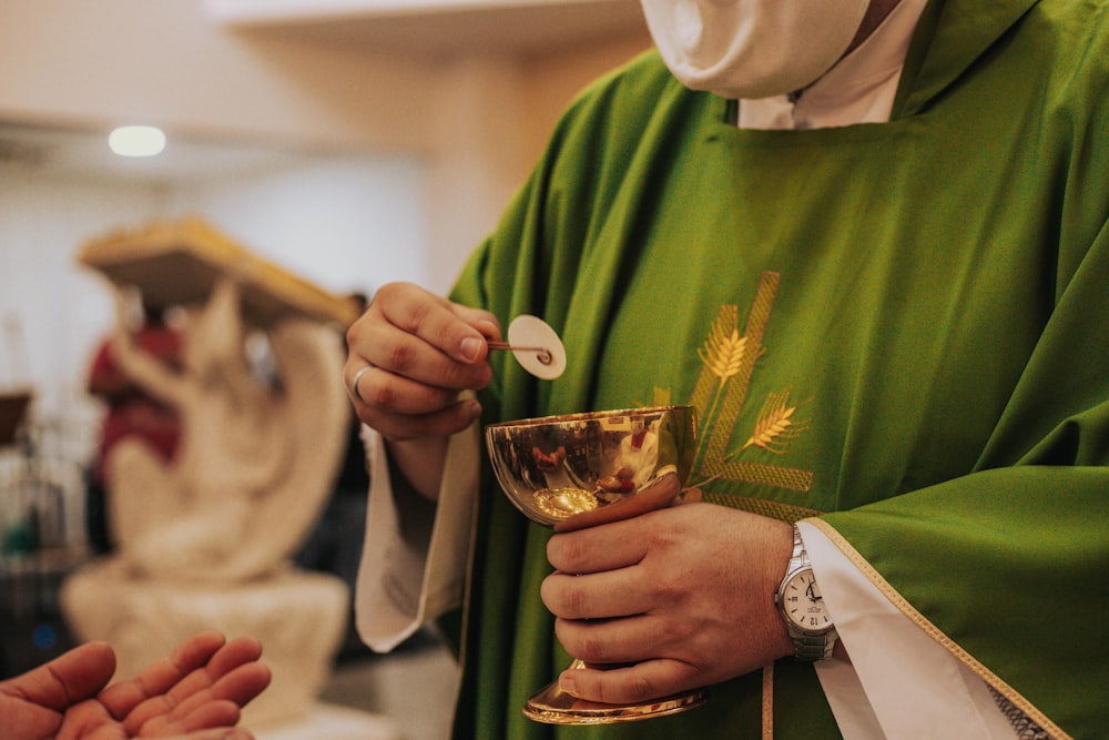 personne en chemise verte à manches longues tenant un verre à boire transparent