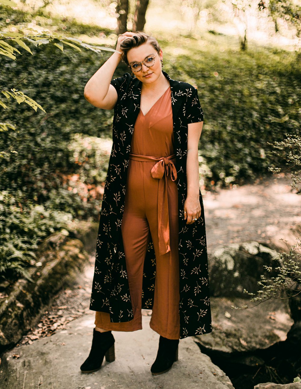 Femme en robe fleurie noire et marron debout près de plantes vertes pendant la journée