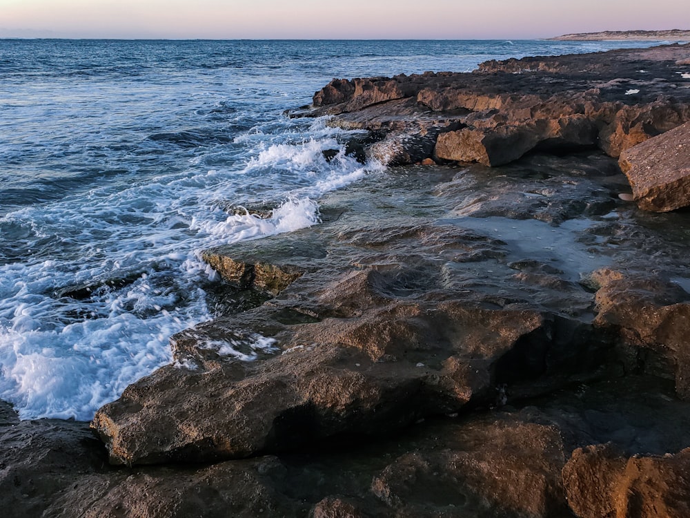 日中に海岸に打ち寄せる海の波がある茶色の岩だらけの海岸