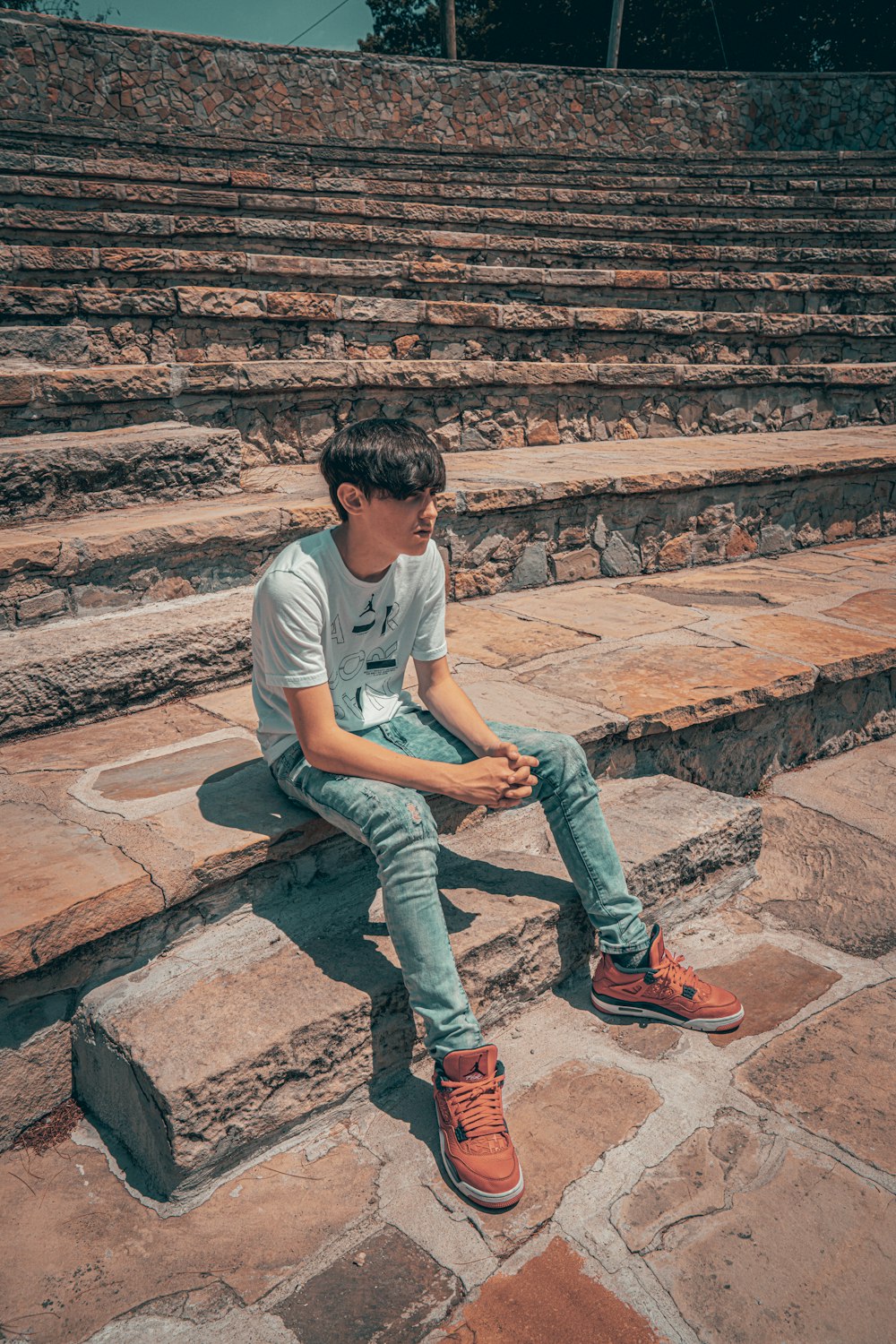 man in white crew neck t-shirt and blue denim jeans sitting on brown concrete stairs