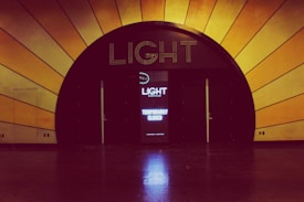 An entrance with a large, dark archway displaying the word 'LIGHT' above closed doors. A sign reads 'TEMPORARILY CLOSED.' The wall features a sunburst pattern in shades of yellow and brown, radiating from the arch.