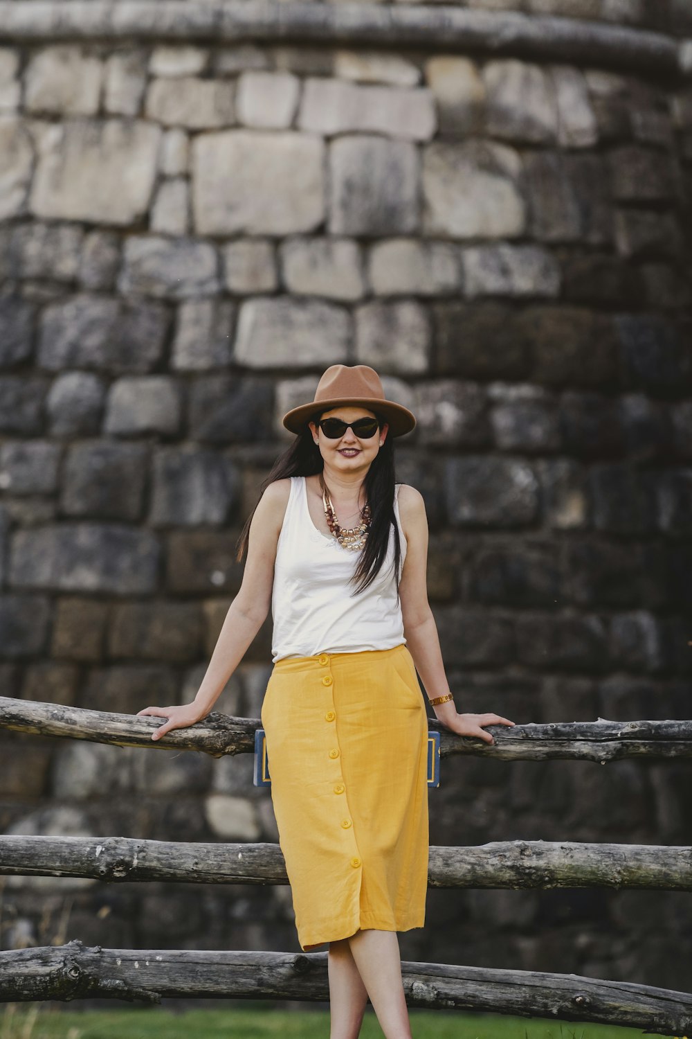 woman in white tank top and yellow skirt wearing brown sun hat standing beside black metal