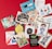 A collection of various greeting cards is displayed on a red background. The cards feature a mix of themes such as sympathy, humor, and birthday wishes. Designs include illustrated animals, flowers, and playful typography. Some cards have witty slogans, while others convey warm sentiments.