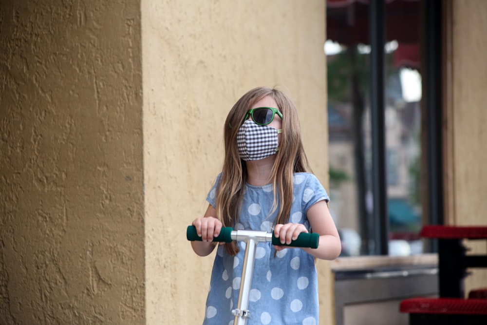 girl in blue and white polka dot dress riding blue bicycle