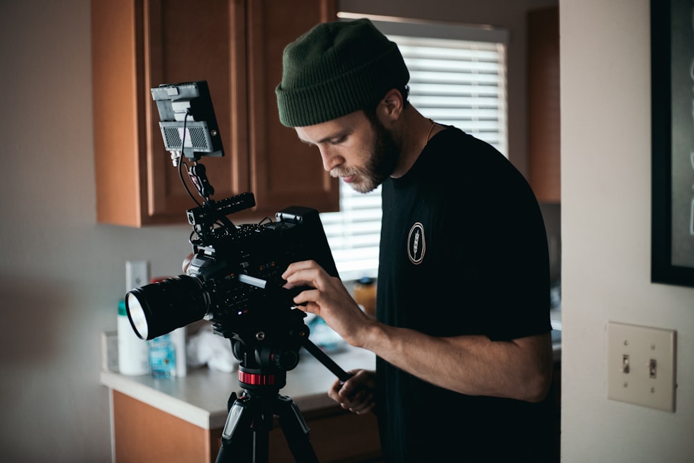 Mann in schwarzem Rundhals-T-Shirt mit schwarzer DSLR-Kamera