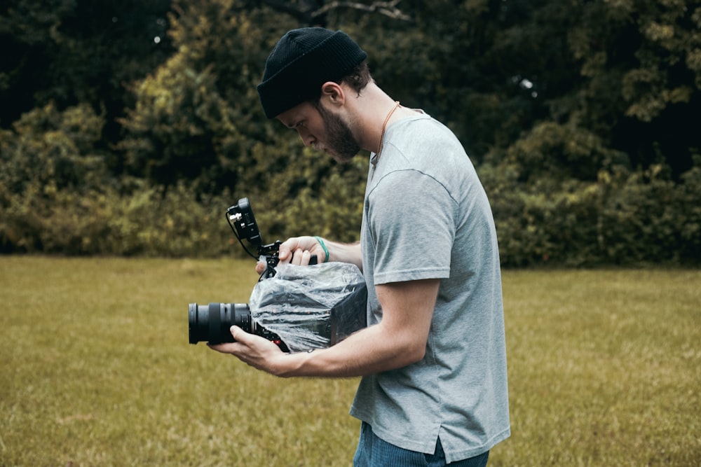 man in gray crew neck t-shirt holding black dslr camera during daytime