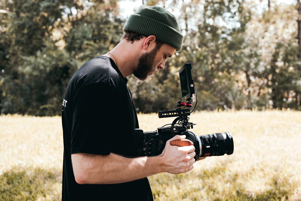 uomo in t-shirt girocollo nera che tiene la fotocamera DSLR nera