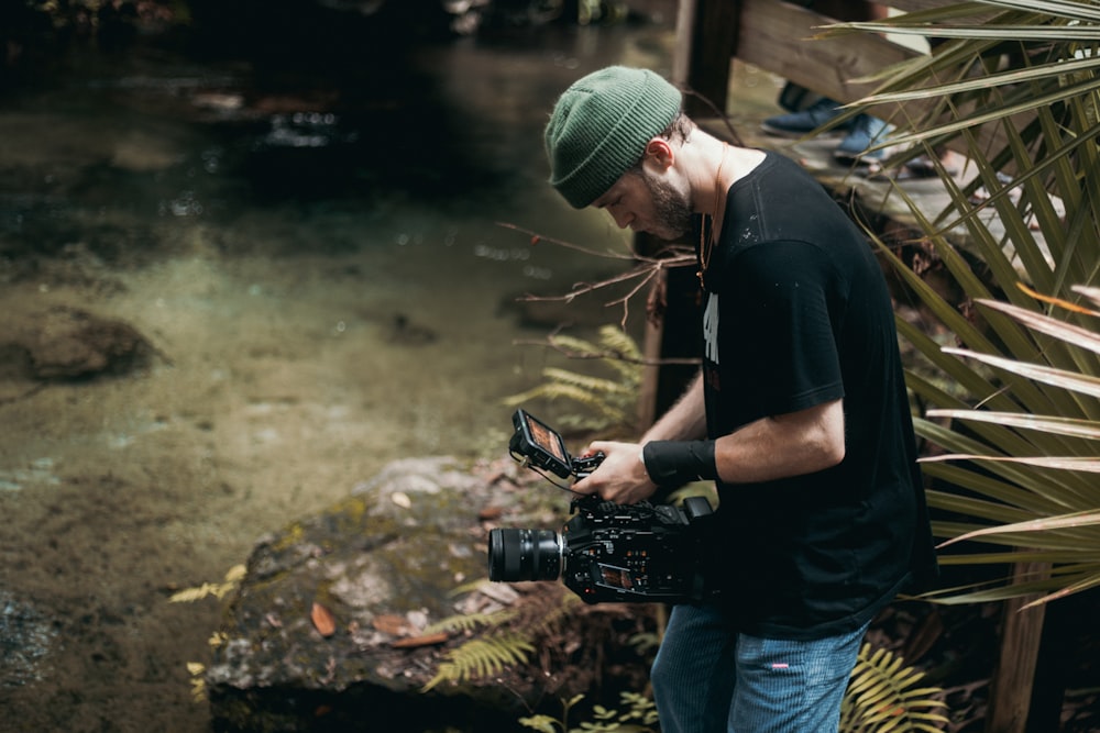 man in black t-shirt and blue denim jeans holding black dslr camera