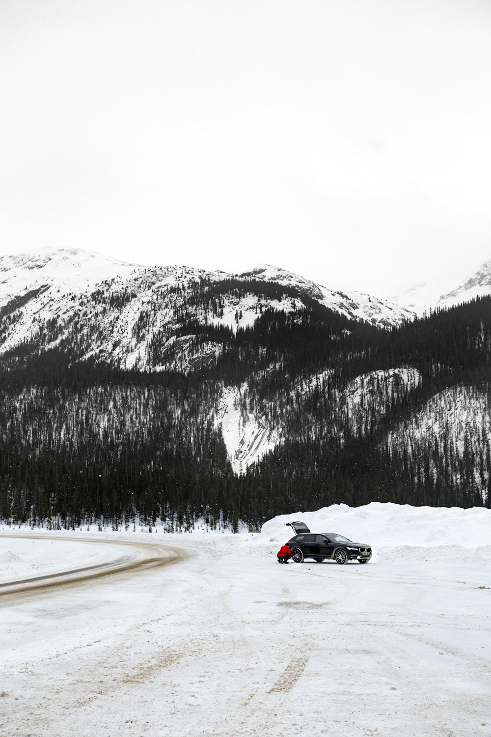 carro esportivo preto e vermelho na estrada coberta de neve perto da montanha coberta de neve durante o dia