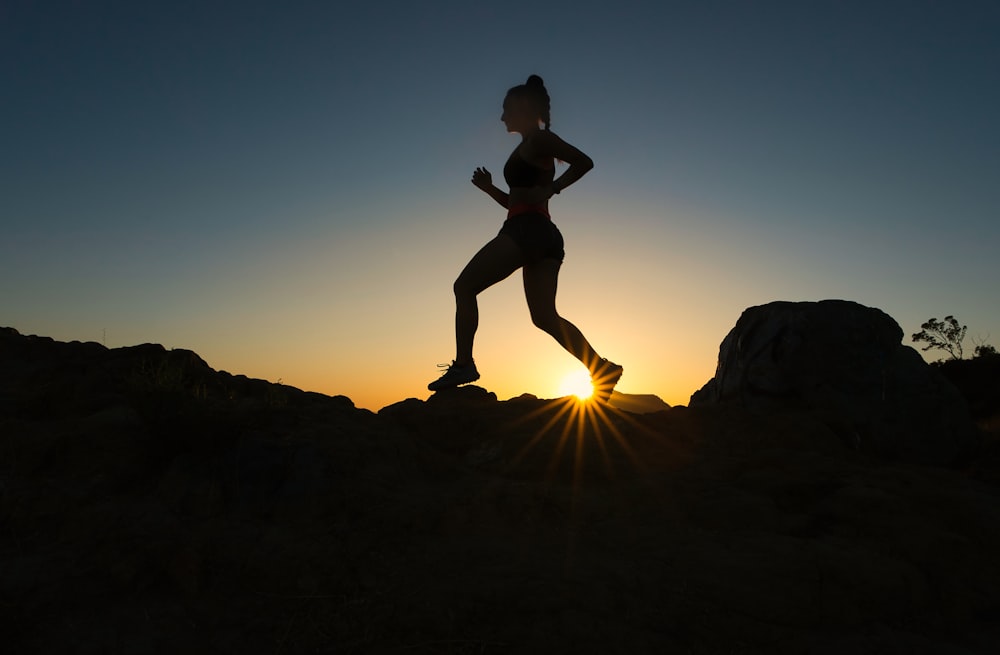 silhouette d’homme sautant sur la montagne rocheuse au coucher du soleil