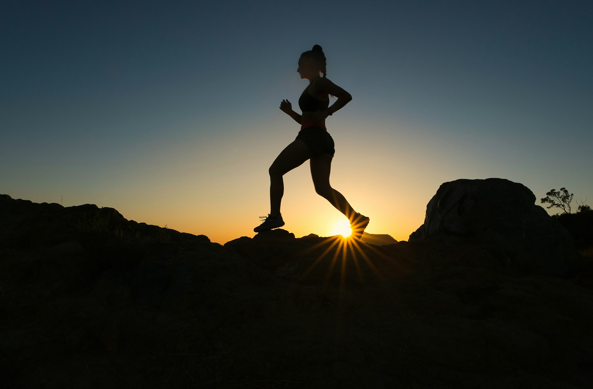 silhouette of woman jumping on rocky mountain during sunset