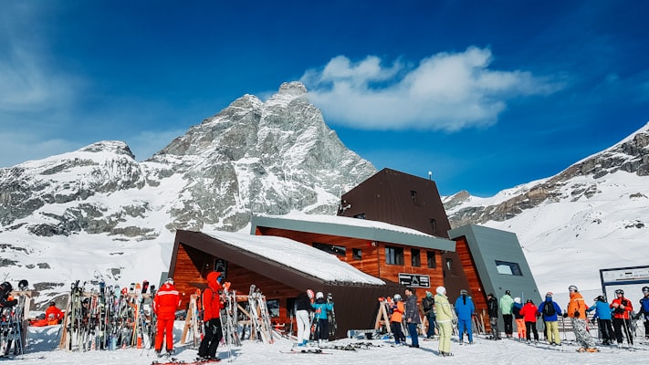 The south face of the Matterhorn, Monte Cervino, rising behind a wooden mountain hut with a crowd of skiers gathered in front