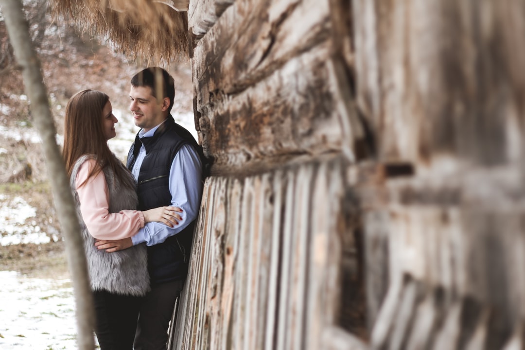 man and woman standing beside brown wooden fence during daytime