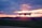 A flying drone captured against a vibrant sunset sky with hues of orange, pink, and purple. The drone is centrally positioned with blurred landscape beneath, suggesting motion and a focus on aerial capabilities.