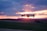 A flying drone captured against a vibrant sunset sky with hues of orange, pink, and purple. The drone is centrally positioned with blurred landscape beneath, suggesting motion and a focus on aerial capabilities.
