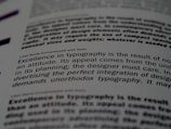 A close-up of a printed page showing text in different fonts and sizes. The visible text discusses typography, mentioning elements like attitude, planning, and the integration of design. The focus is on one sentence and the text around it is blurred.