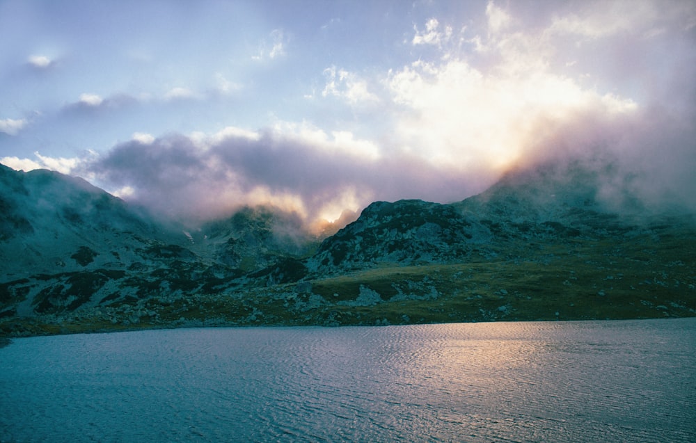 green mountain beside body of water under cloudy sky during daytime