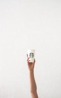 Hands with elegant, minimalist press-on nails holding a cup of coffee by a sunlit window.