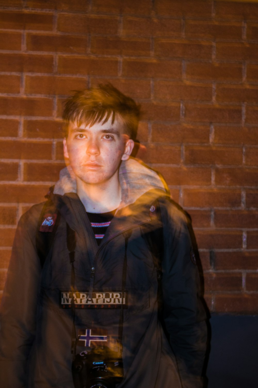 man in black leather jacket standing beside brown brick wall