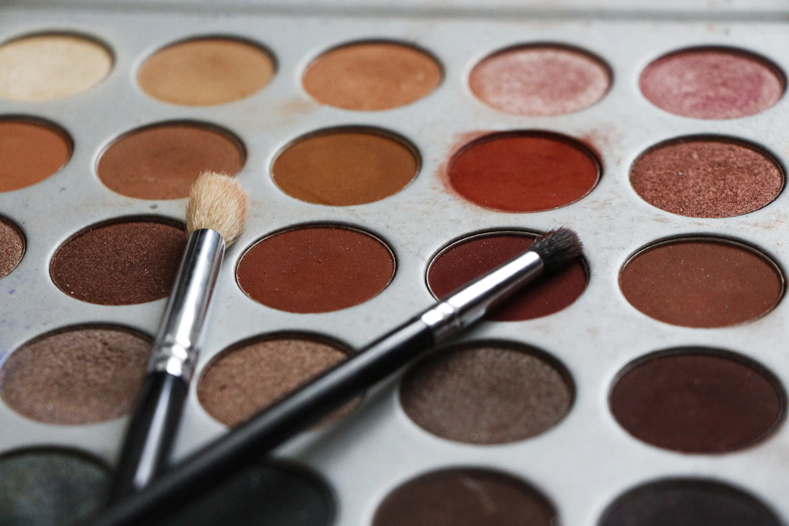 Palette de fards aux teintes brunes et deux pinceaux de maquillage