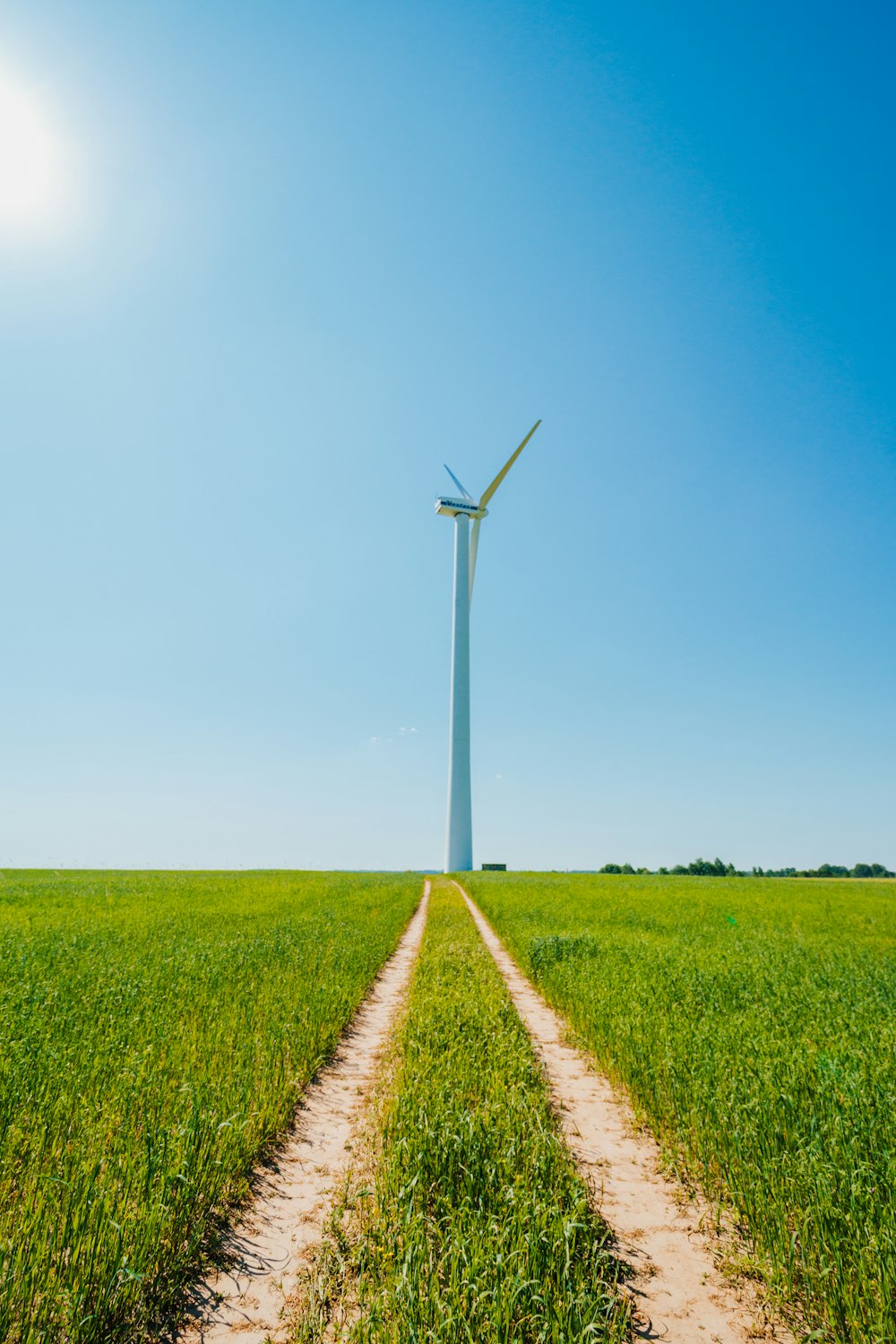 white wind turbine on green grass field under blue sky during daytime