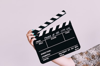 A film clapperboard is being held by a person with painted nails and leopard print clothing. The clapperboard is labeled 'Church of the City NYC' and contains spaces for production details such as 'Roll,' 'Scene,' and 'Take.'