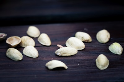Scattered pistachio nuts are positioned on a dark wooden surface. The nuts appear to be raw and some have half-opened shells.
