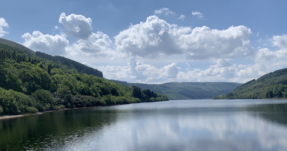 green mountains beside body of water under white clouds during daytime