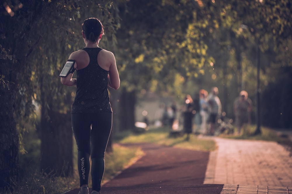 woman in black tank top and black pants walking on sidewalk during daytime