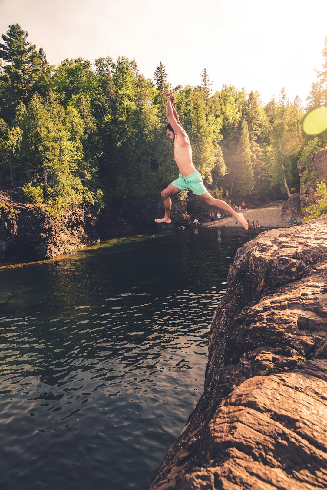 woman in pink bikini jumping on brown rock near body of water during daytime