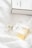 A clear glass perfume bottle labeled with 'N°5 CHANEL PARIS EAU DE PARFUM' rests on a soft white fabric. In the background, there is a matching rectangular box with similar branding. The bottle contains a light amber liquid.