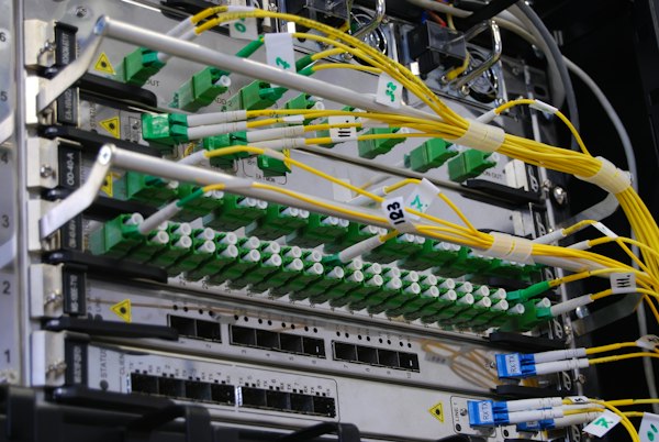 Cabos de fibra ótica ligados a um switch de rede num armário de telecomunicações