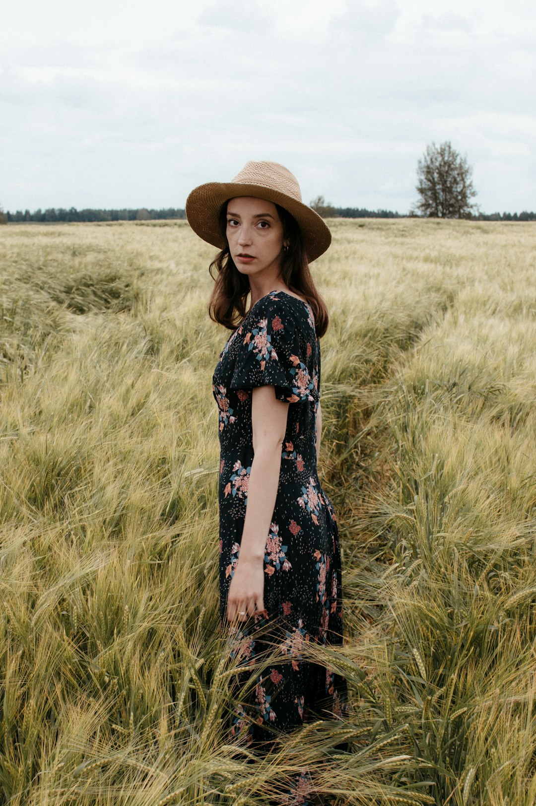 woman in black and white floral dress wearing brown straw hat standing on green grass field