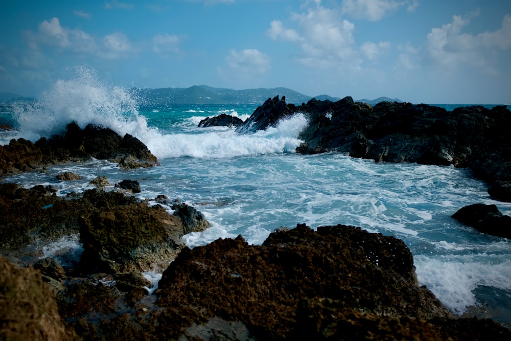 Olas oceánicas rompiendo en la formación rocosa marrón bajo el cielo azul durante el día