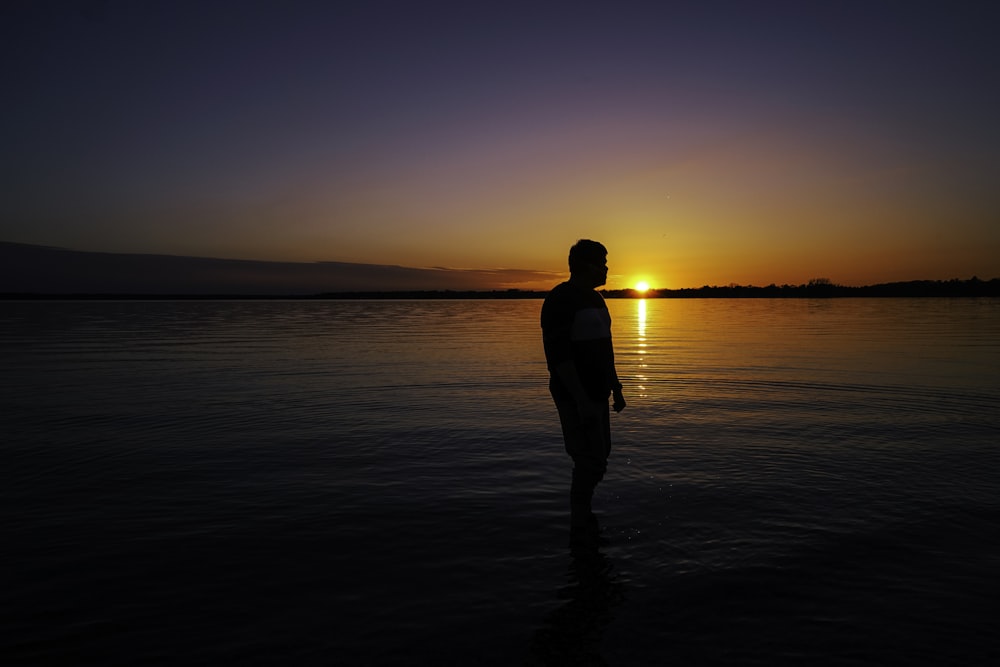 silhouette of man standing on seashore during sunset