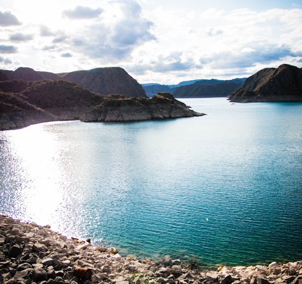 blue lake surrounded by mountains under white clouds and blue sky during daytime