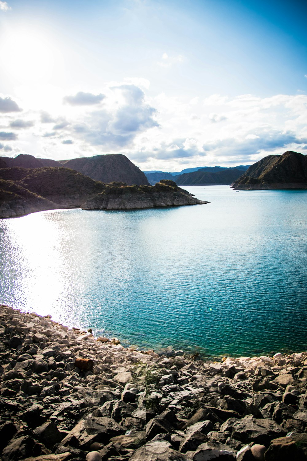 blue lake surrounded by mountains under white clouds and blue sky during daytime