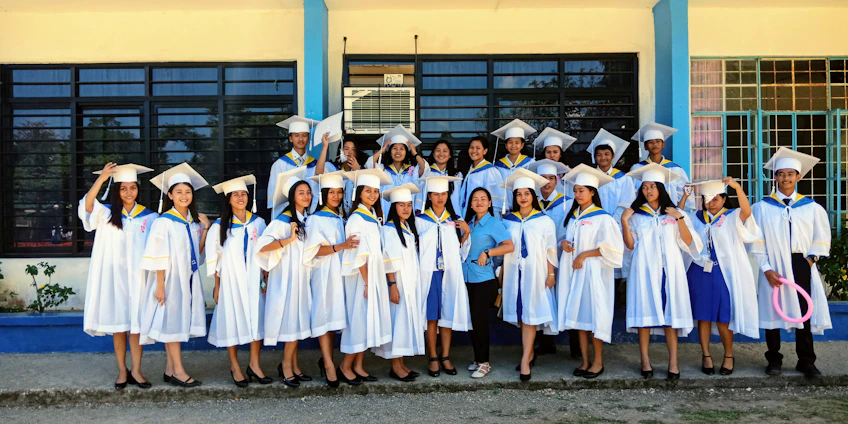 A diverse group of smiling students in graduation robes standing in front of a modern college building, representing success and new beginnings.