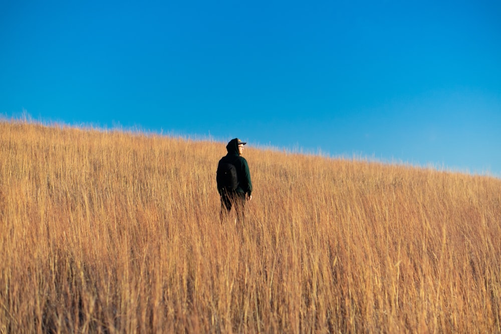 昼間、茶色の芝生の上に立つ黒いジャケットの男