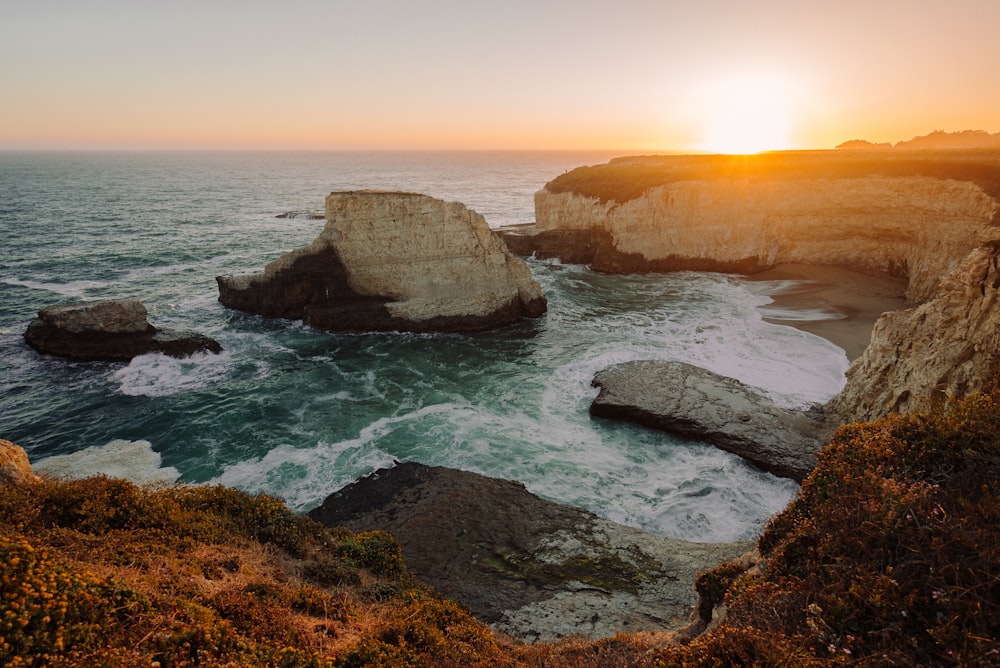 formação rochosa marrom no mar durante o pôr do sol
