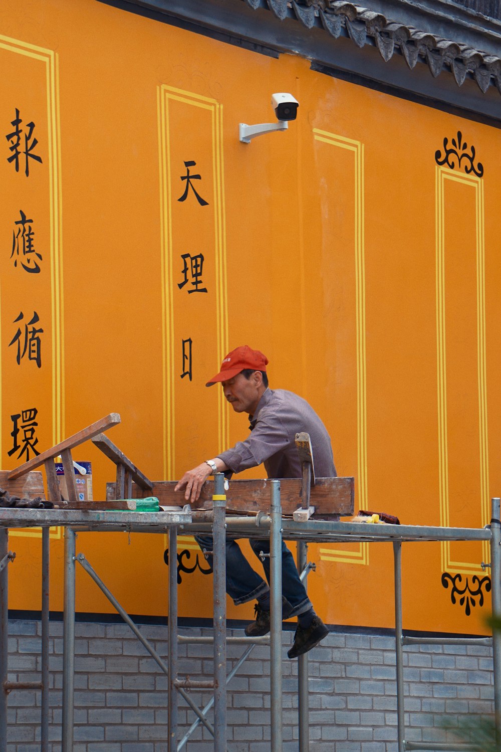 man in grey long sleeve shirt and orange cap sitting on blue metal bar