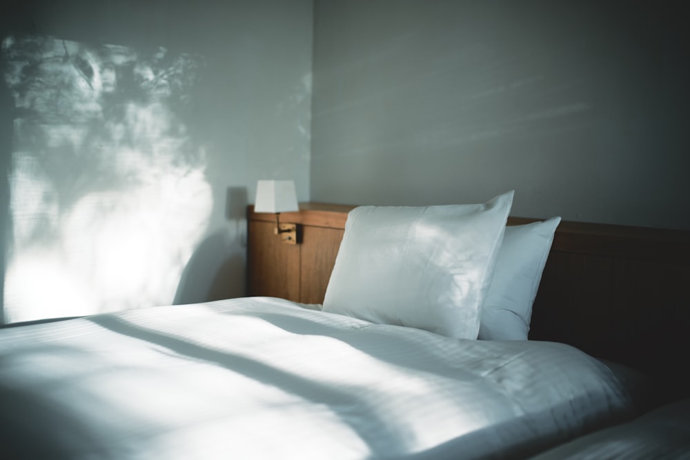 white bed linen beside brown wooden nightstand