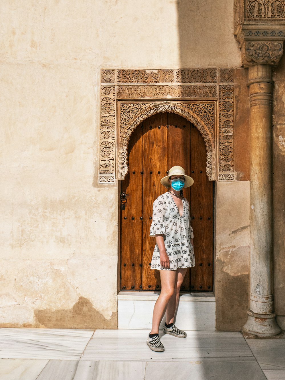 woman in white and blue floral dress standing in front of brown wooden door