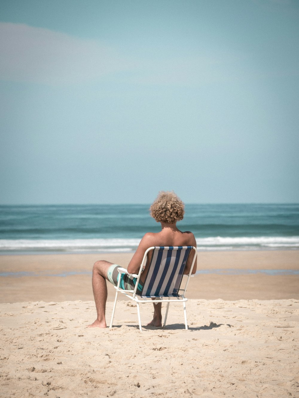 woman in red dress sitting on white and blue chair on beach during daytime