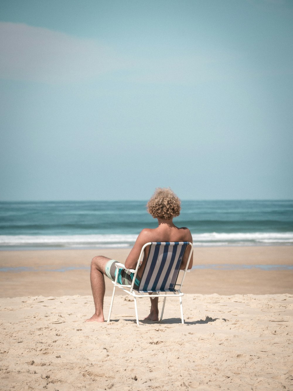 donna in vestito rosso che si siede sulla sedia bianca e blu sulla spiaggia durante il giorno