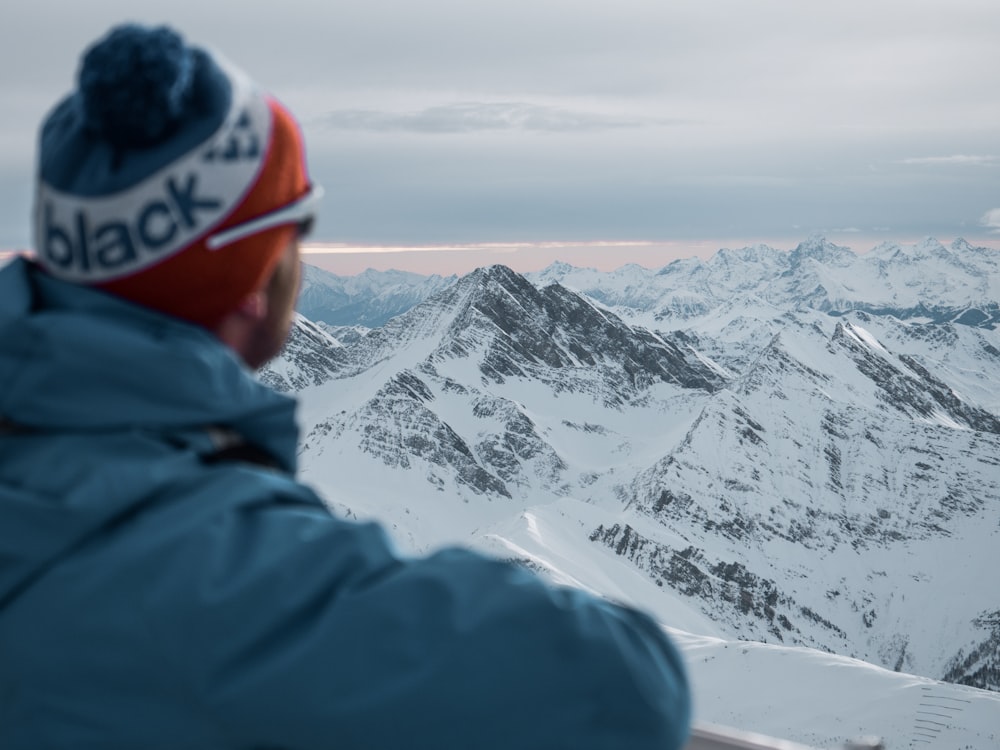 person in blue jacket and red cap standing on snow covered mountain during daytime