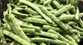 A close-up view of a large pile of fresh, green beans with a bright and even green color and smooth texture. The beans are stacked on top of each other in a seemingly random arrangement.