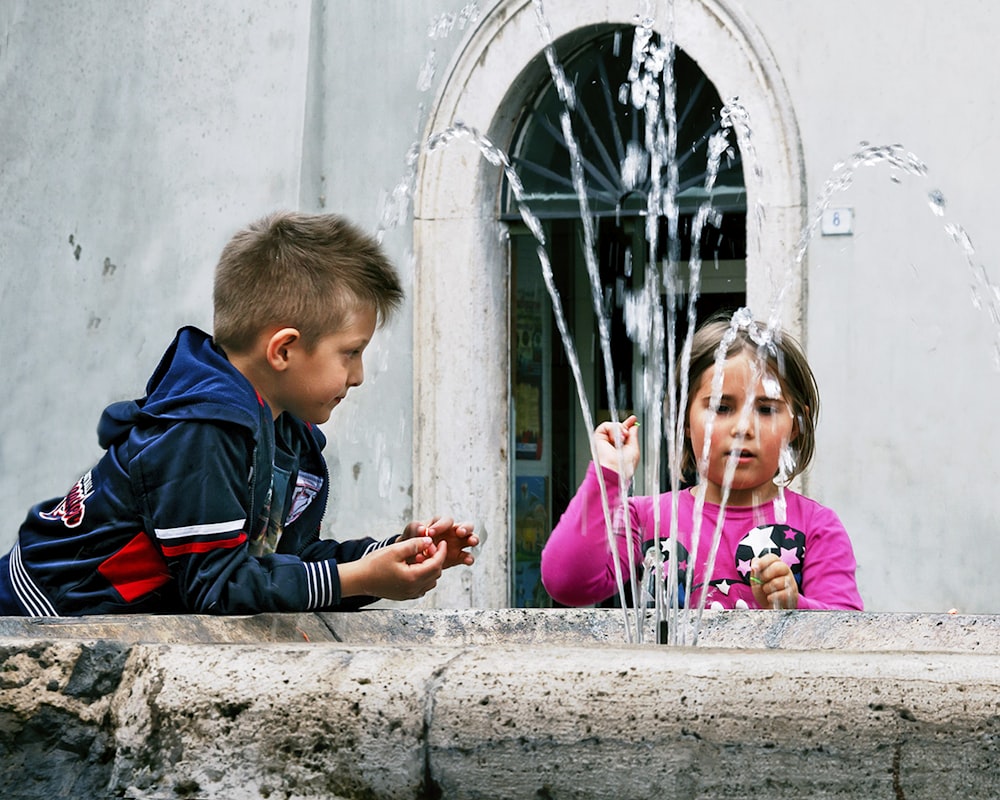 boy and girl sitting on concrete bench during daytime