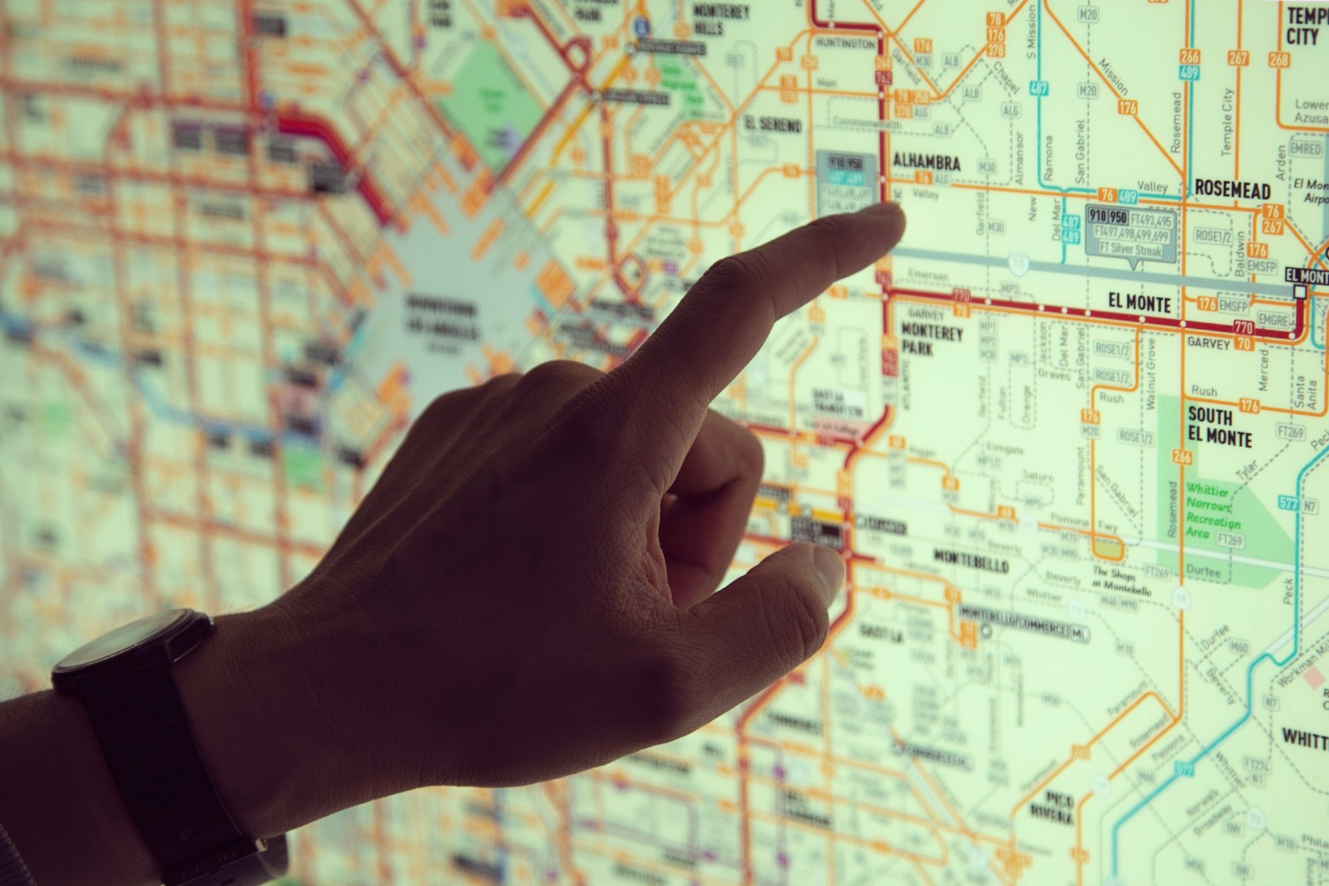 Left hand pointing at a screen displaying a transit map with routes and transfer points.