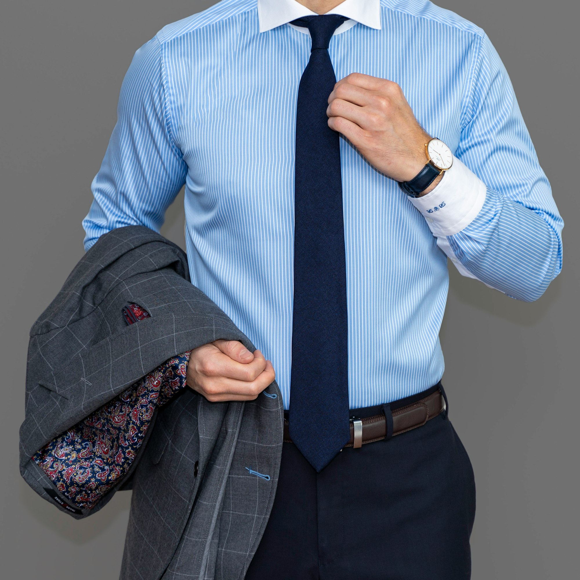 Dapper Professional wearing a custom shirt featuring a blue pinstripe with contrasting cuffs and wide spread collar. He's wearing a solid blue tie and holding a custom blazer. 